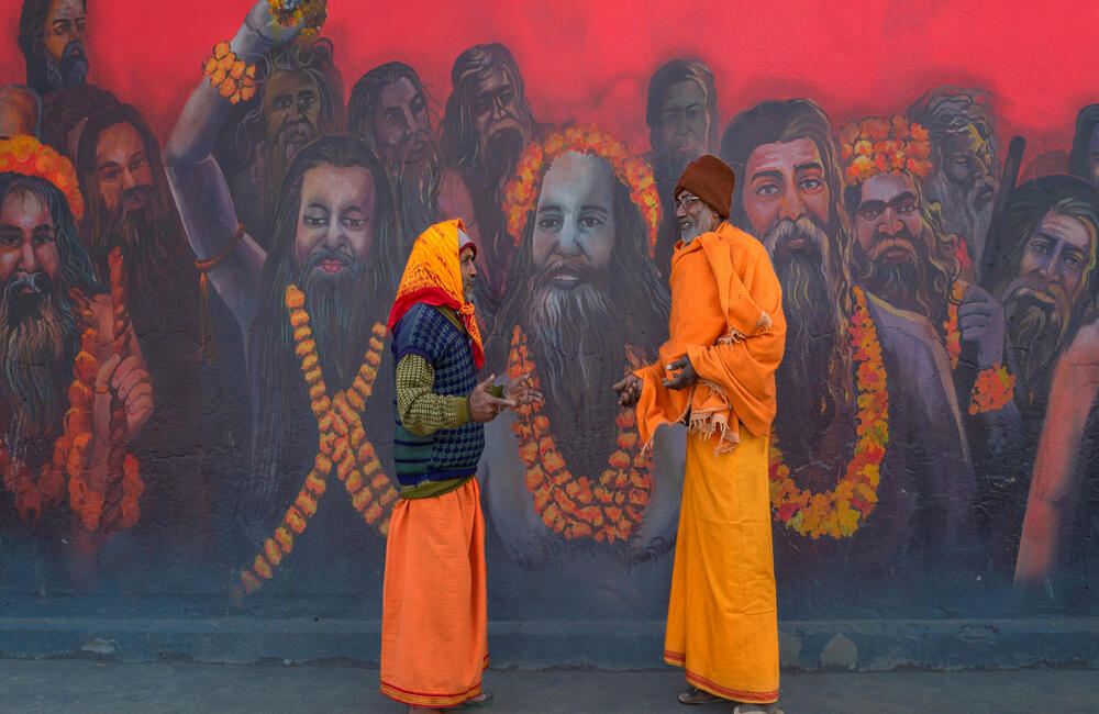 A meeting of two sadhus against a backdrop of a colourful wall painting of Naga sadhus at the Prayag Kumbh, 2019. Kumbh has a deep religious and spiritual significance in Hindu cosmology but the social dimension that is attached to it cannot be ignored. The pilgrim or the sadhu also travels to the Kumbh to meet and socialize with other fellow beings.  Photographer: Senthilkumar Kandhakrishnan.